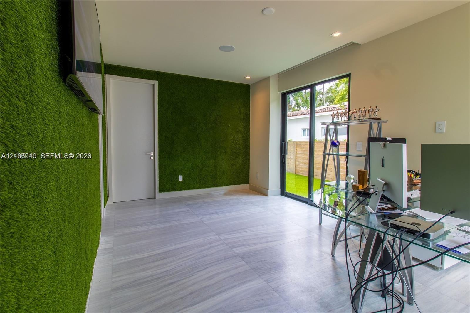Room featuring textured green wall cladding, neutral large-format tile flooring, recessed ceiling lighting, and sliding glass doors with exterior acce