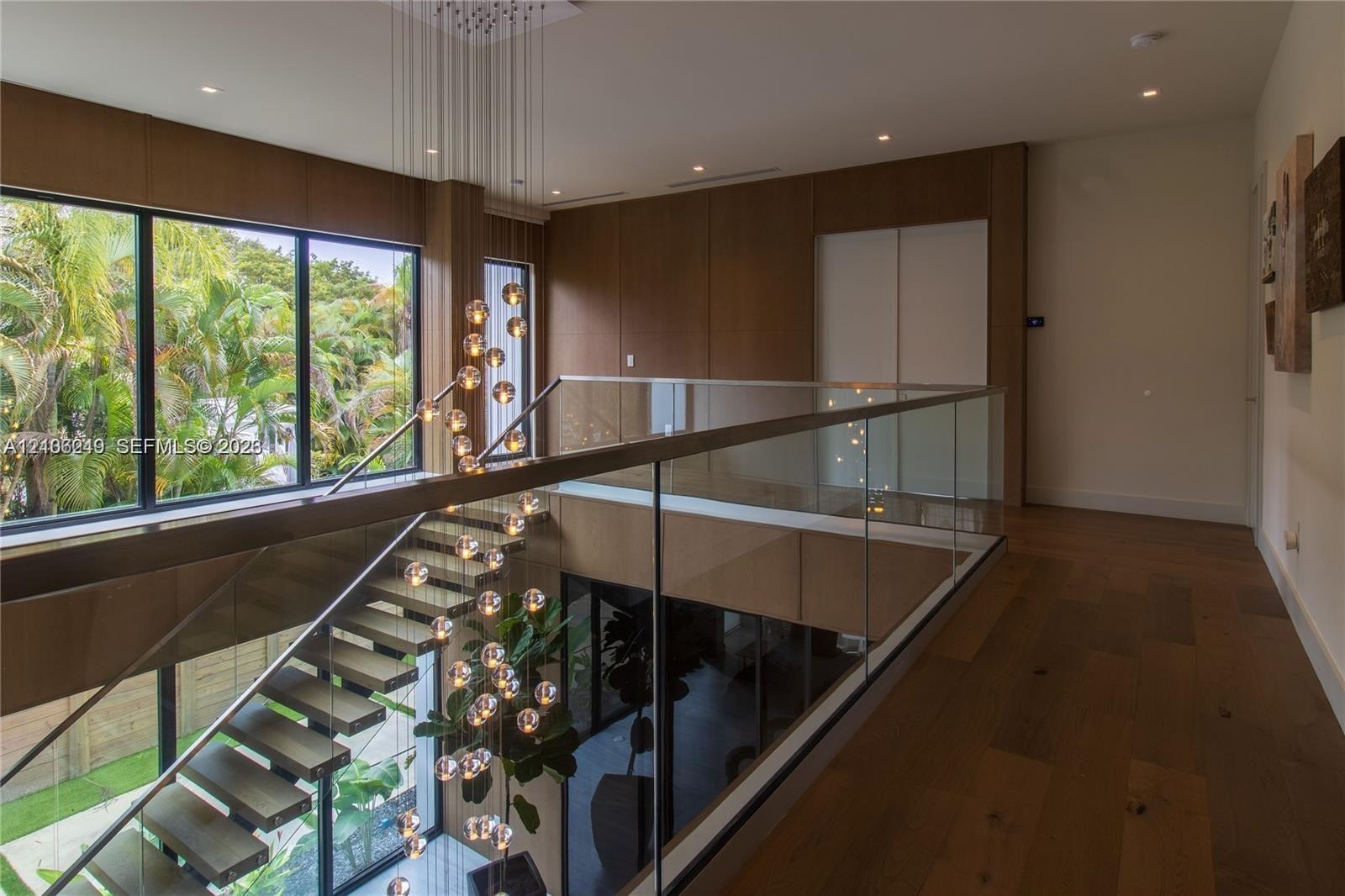 Floating staircase with wood treads and glass railing, large-format wood-finish wall paneling, floor-to-ceiling windows, recessed lighting, and wood-f