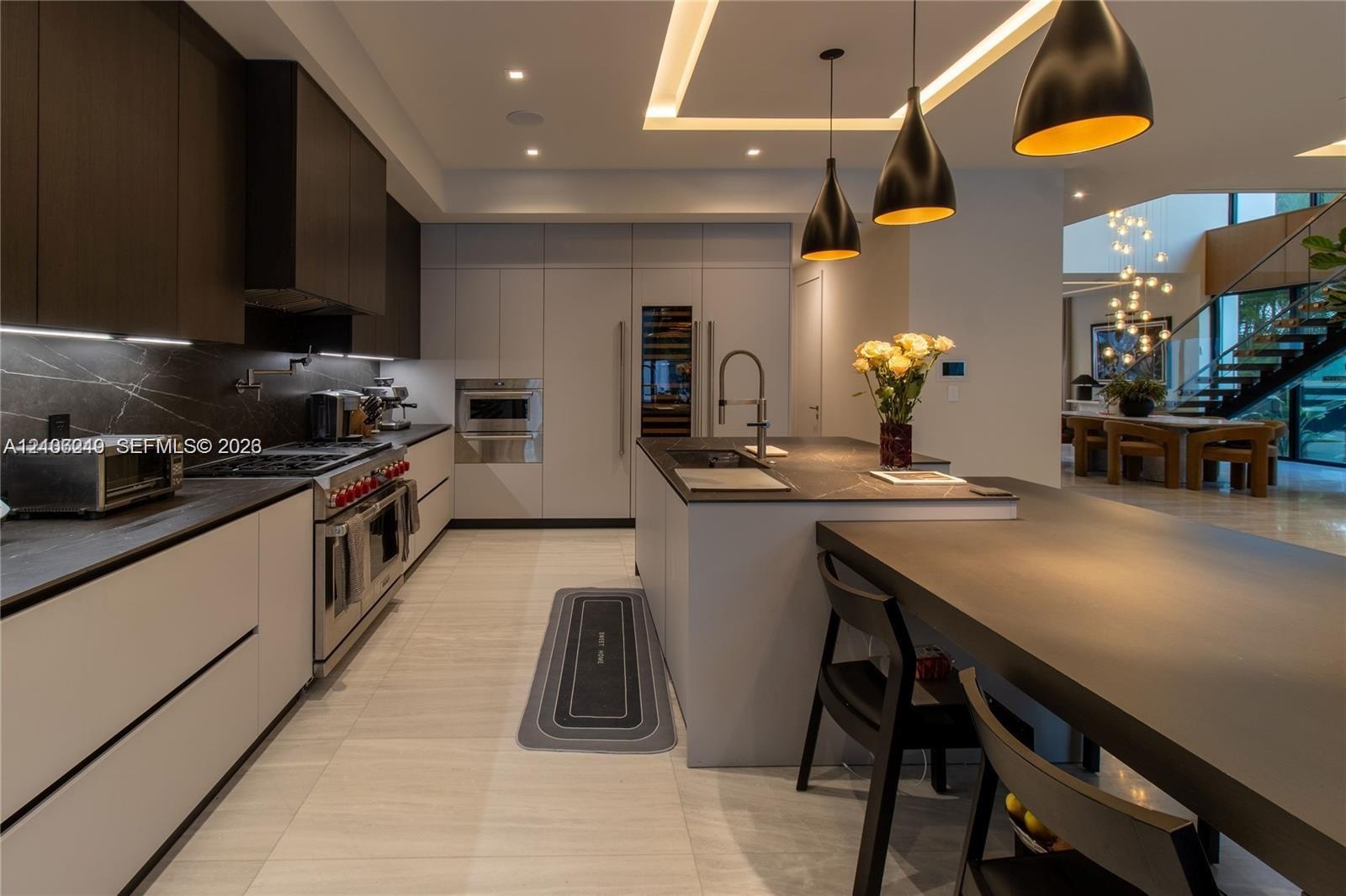 Modern kitchen featuring custom flat-panel cabinetry, dark stone-finish countertops, built-in stainless steel appliances, a large central island with 