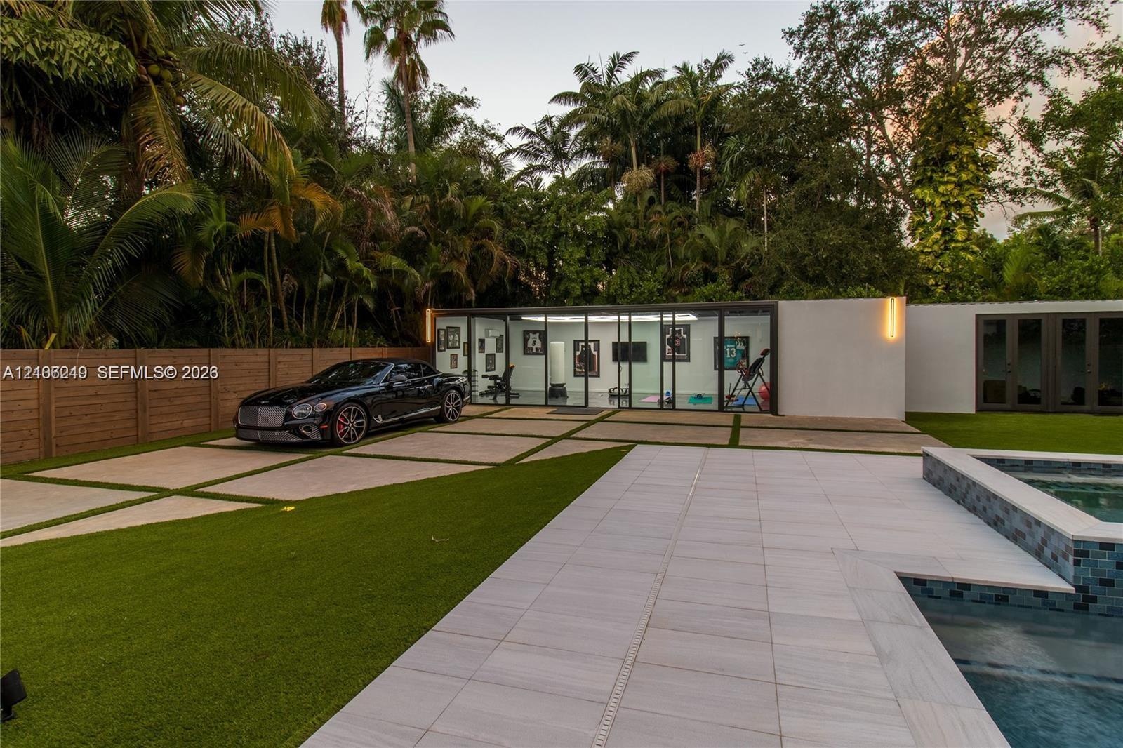 Contemporary pool deck featuring large-format stone pavers, integrated glass-walled studio structure, geometric concrete driveway with turf inserts, a