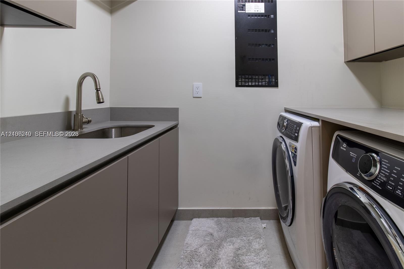Utility room featuring matte-finish cabinetry, stone-composite countertops, an integrated stainless steel sink with a high-arch faucet, and overhead s