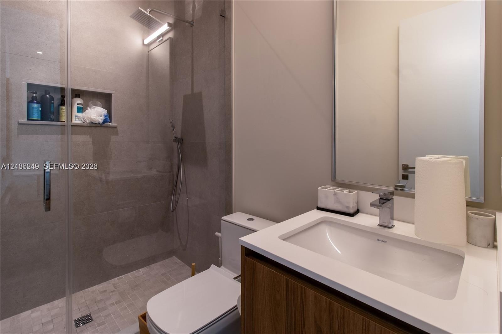 Bathroom featuring a glass-enclosed walk-in shower with stone tile, a built-in recessed niche, rainfall showerhead, wood-finish vanity with an integra