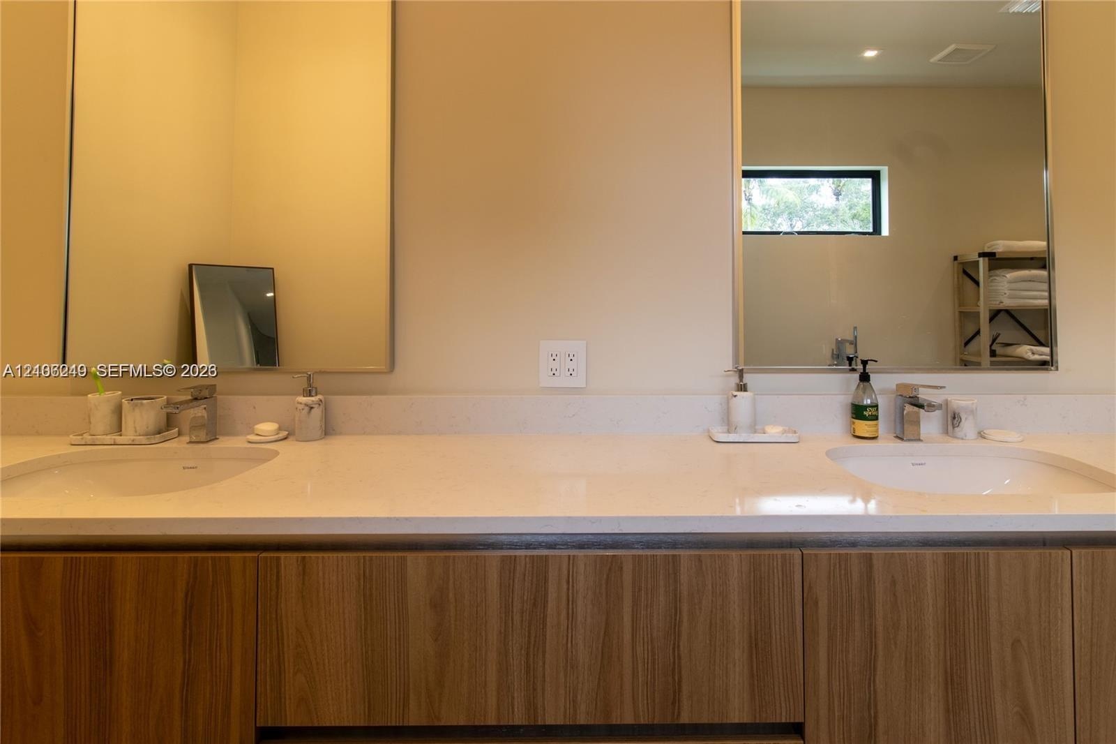 Double vanity featuring a light-toned solid surface countertop, wood-finish cabinetry, two undermount sinks with polished chrome faucets, and dual int