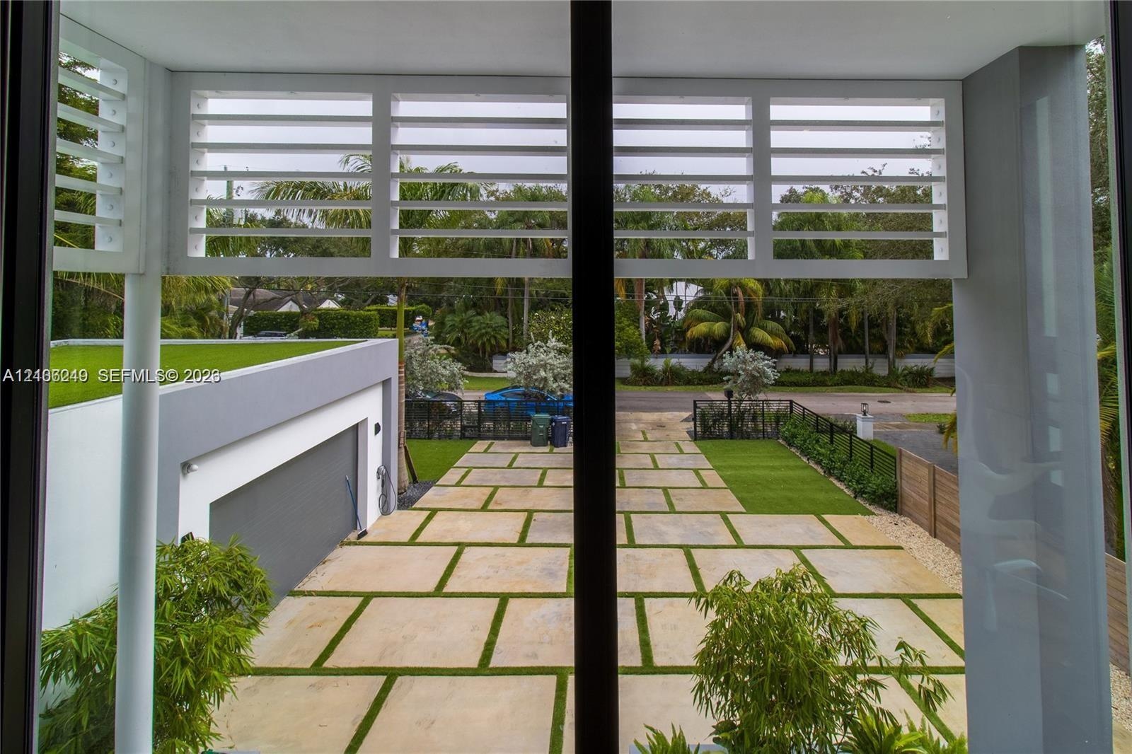 Exterior covered balcony featuring horizontal slatted privacy screens, overlooking a geometric paver driveway with turf accents and a modern flat-roof