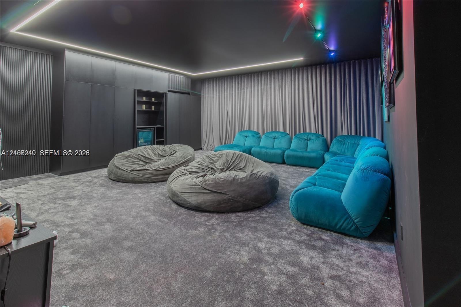 Media room featuring floor-to-ceiling built-in cabinetry, recessed LED perimeter lighting, charcoal-toned wall finishes, and wall-to-wall carpeting
