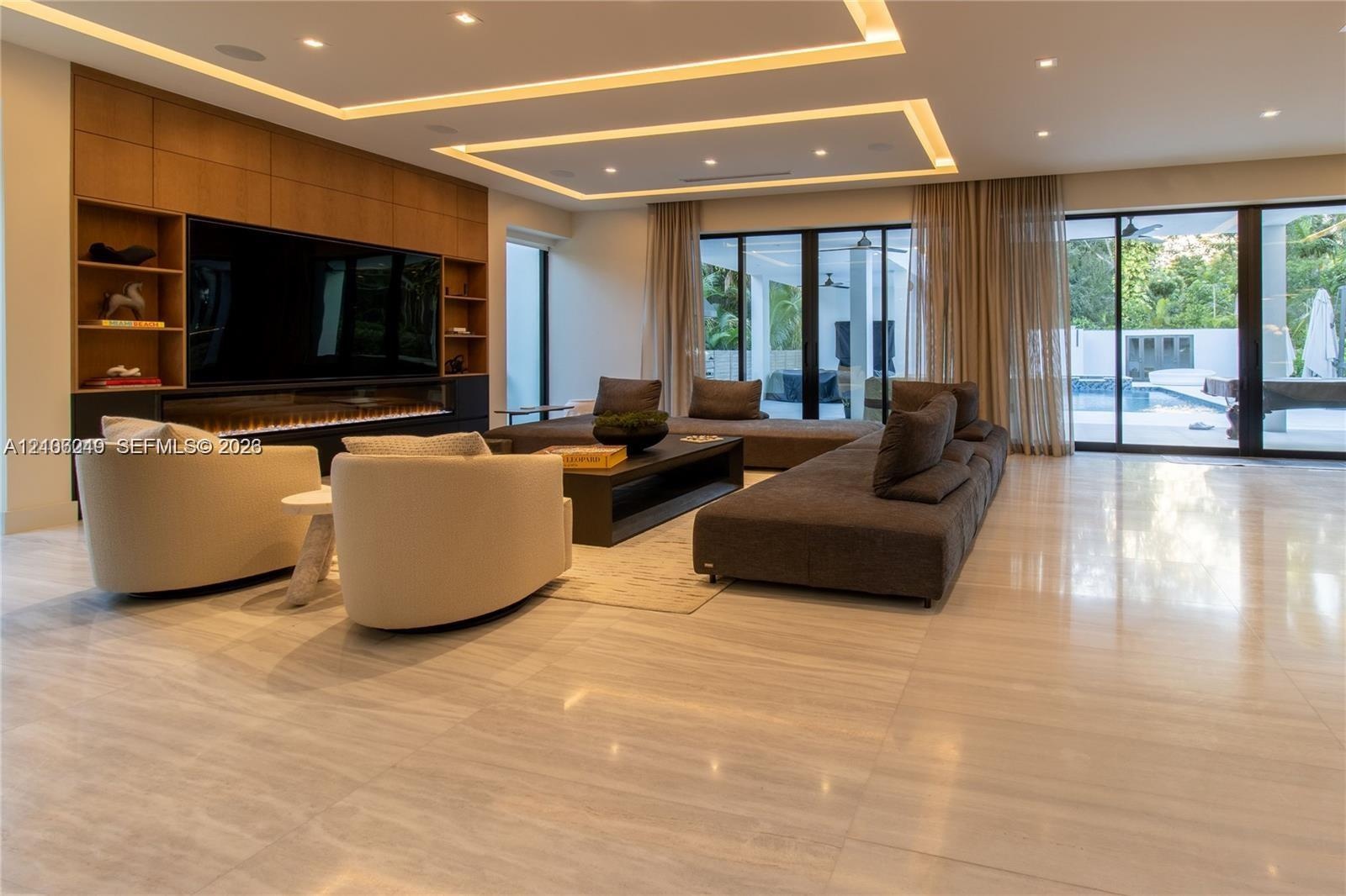 Large-format stone tile flooring, built-in wooden cabinetry with integrated shelving, linear fireplace, recessed tray ceiling with cove lighting, and 