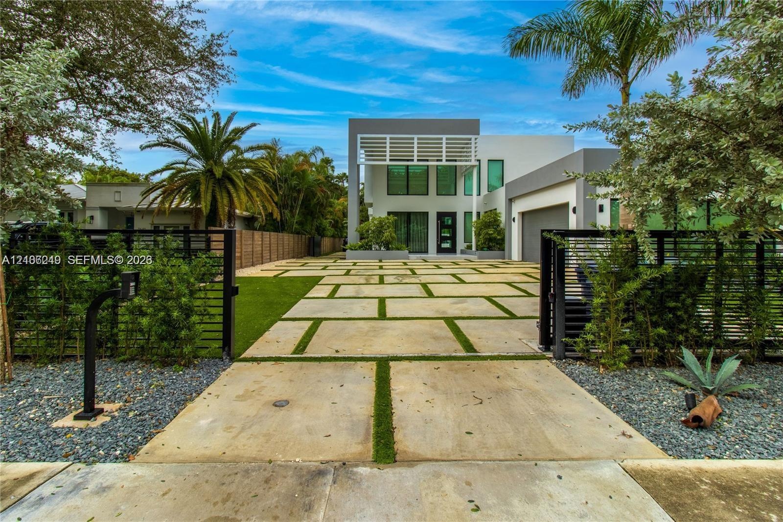 Modern two-story exterior featuring a geometric concrete paver driveway with turf inlays, a white louvered architectural overhang, expansive vertical 