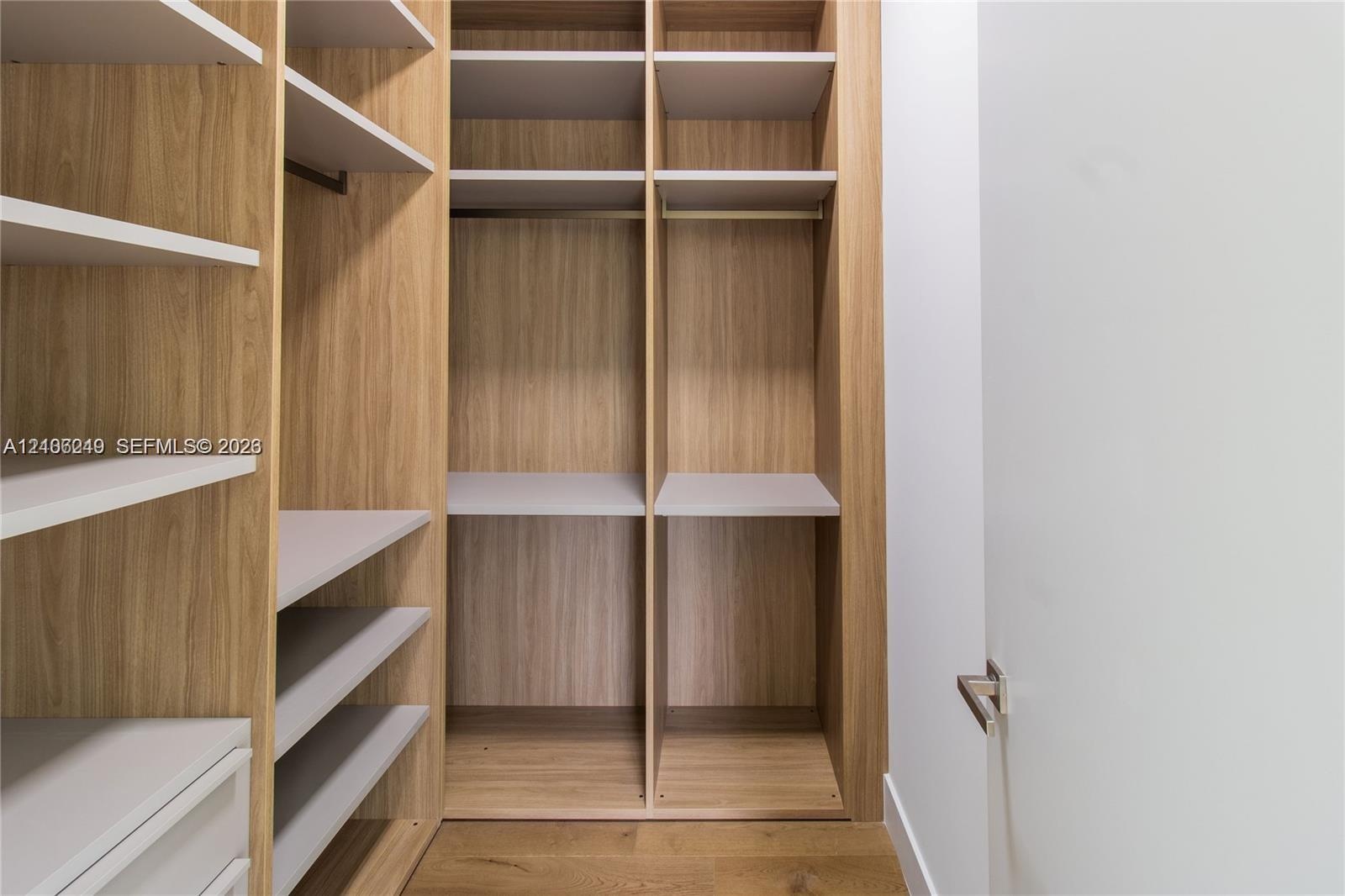 Customized walk-in closet featuring floor-to-ceiling wood-finish shelving, multi-level hanging rods, built-in drawer units, and wood-finish flooring
