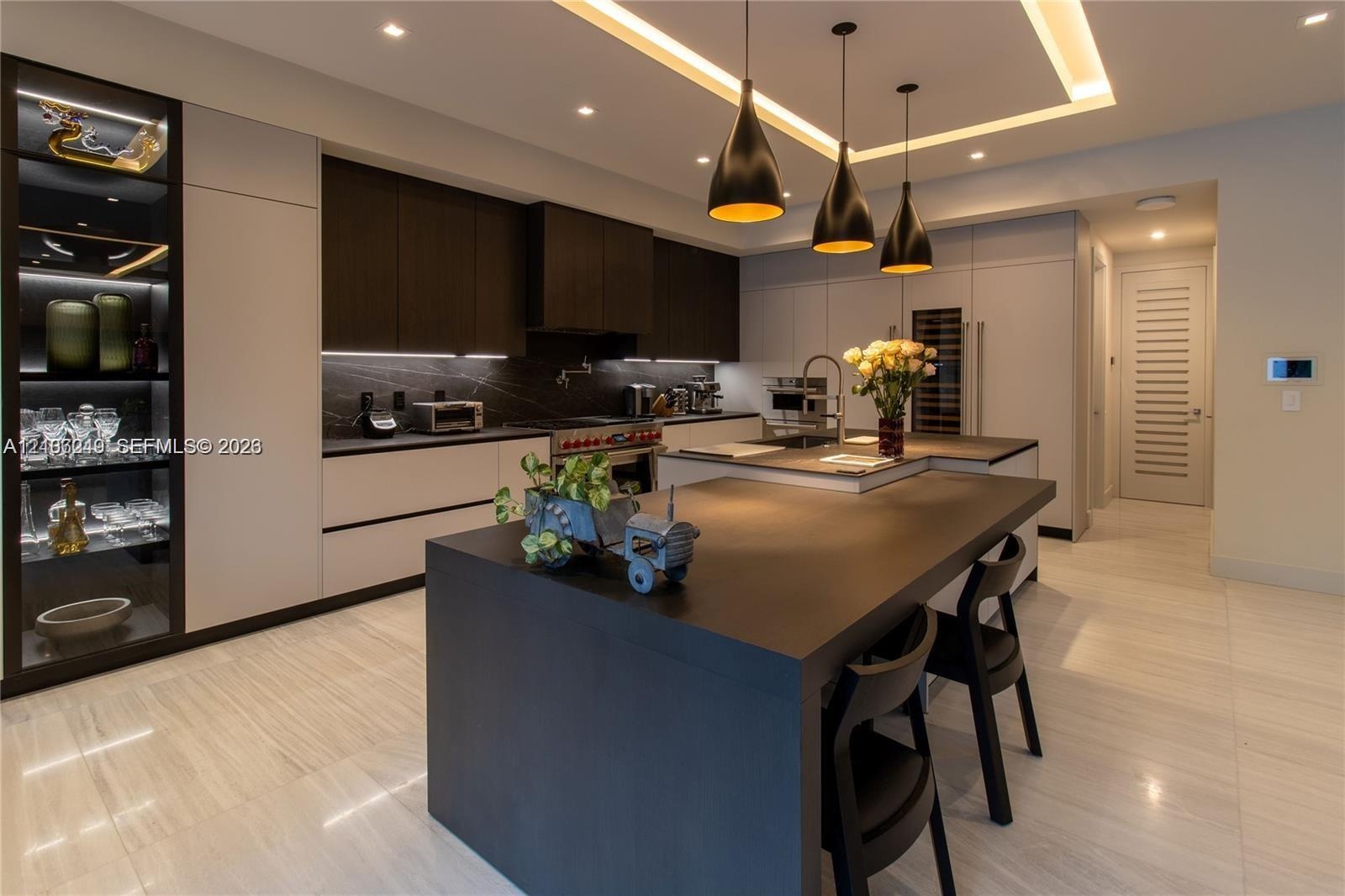 Gourmet kitchen featuring flat-panel cabinetry, a central waterfall-edge island, stone-surfaced countertops, custom recessed tray ceiling lighting, an