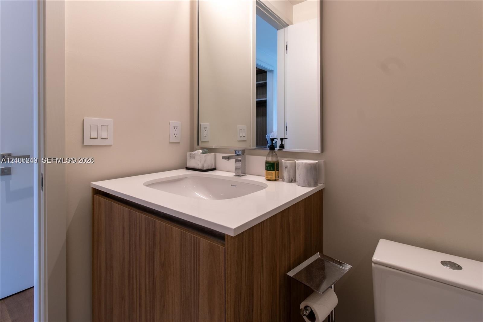 Wood-finish vanity cabinet with a white countertop, integrated sink, polished chrome faucet, and rectangular wall-mounted mirror