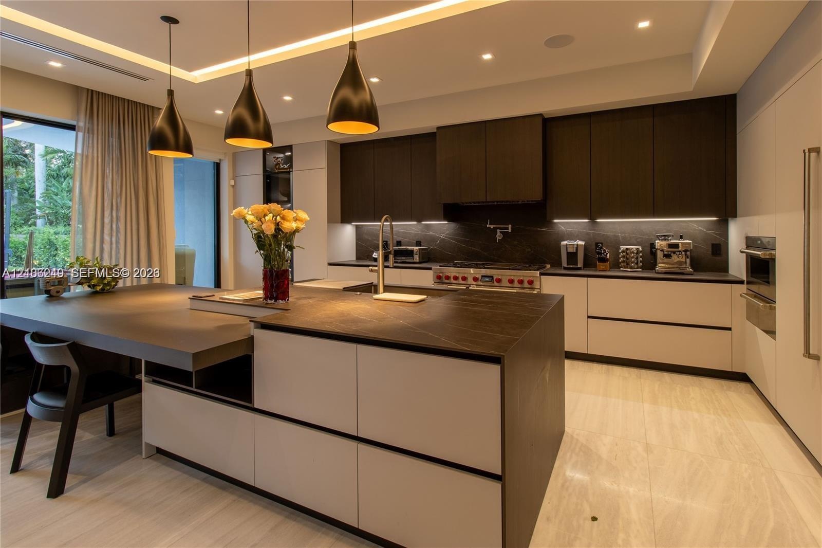 Gourmet kitchen featuring a large central island with stone-finish countertops, matte-finish cabinetry, built-in dual wall ovens, and custom pendant l