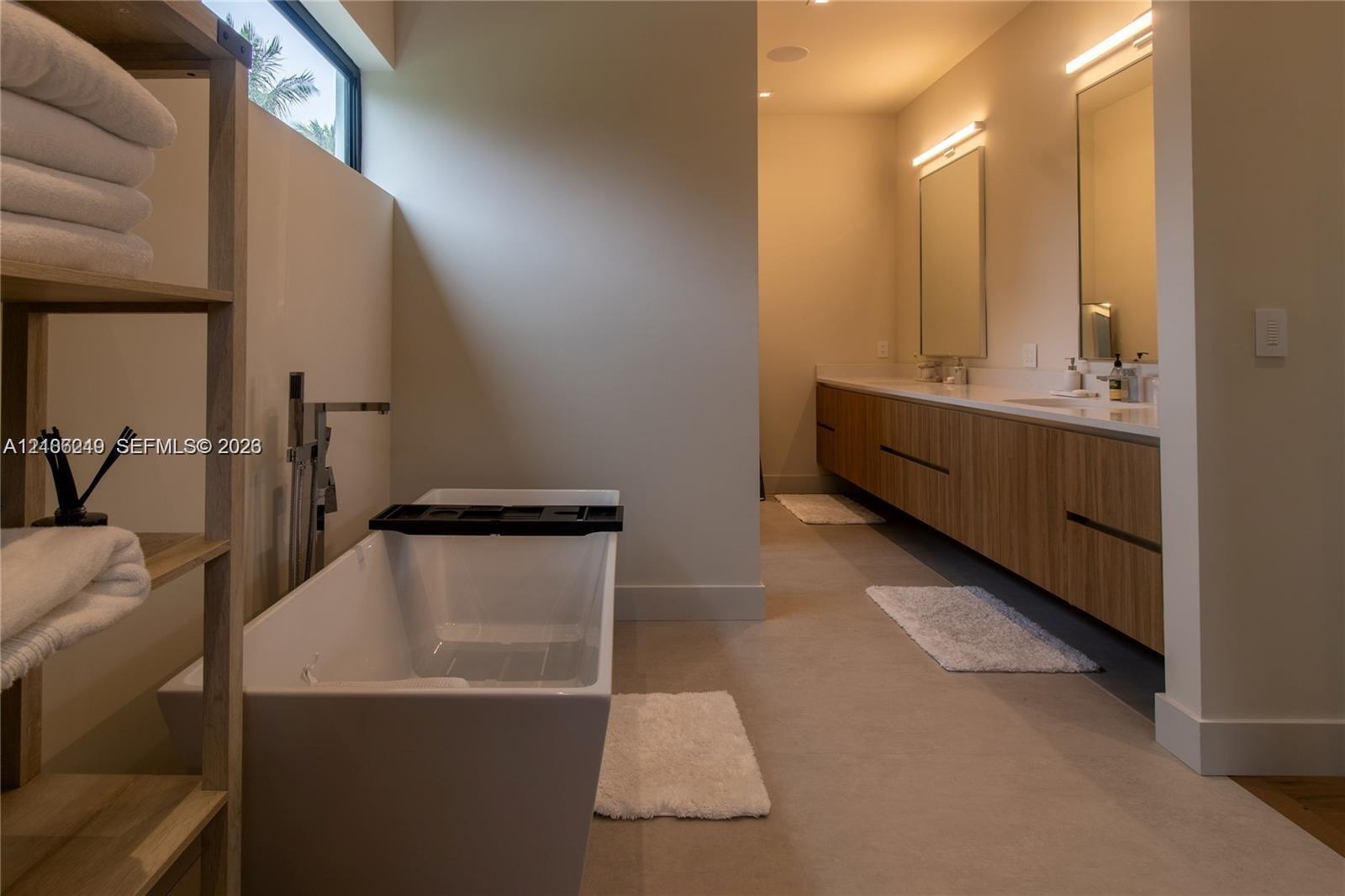 Freestanding soaking tub with floor-mounted faucet, dual-sink floating vanity with wood-finish cabinetry, countertop-to-ceiling mirrors, integrated wa