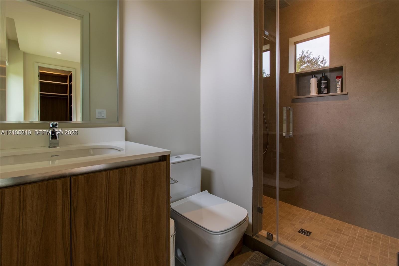 Bathroom featuring a wood-finish vanity with an integrated sink, large frameless mirror, glass-enclosed shower with tiled flooring, and a built-in sho