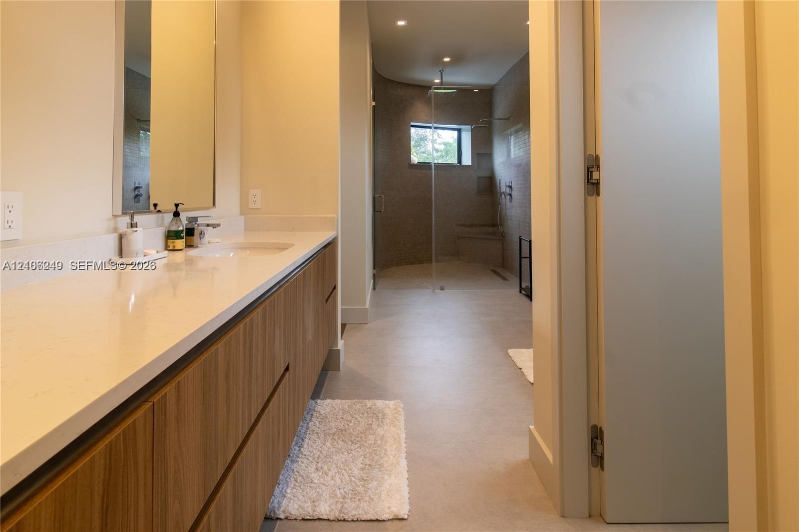 Floating vanity with a wood-finish, integrated countertop with a sink, large frameless mirror, and a walk-in shower with tiled walls and a built-in be