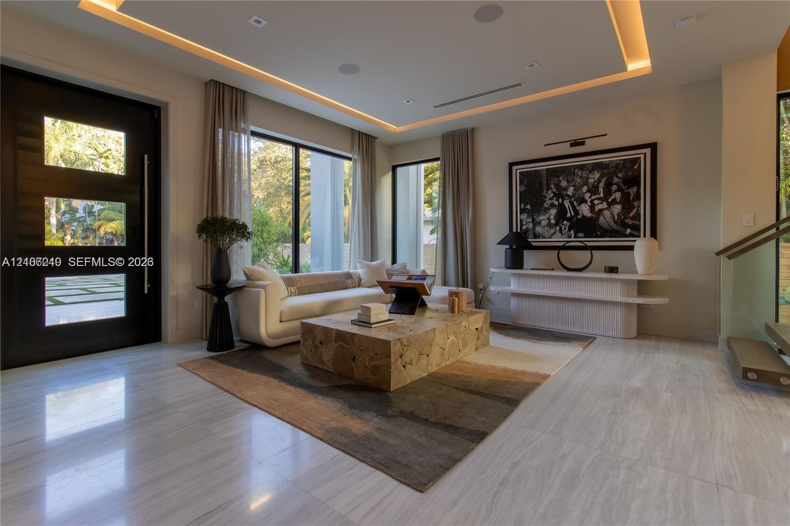 Contemporary interior featuring polished stone flooring, recessed tray ceiling with integrated perimeter lighting, large-format glass windows with bla