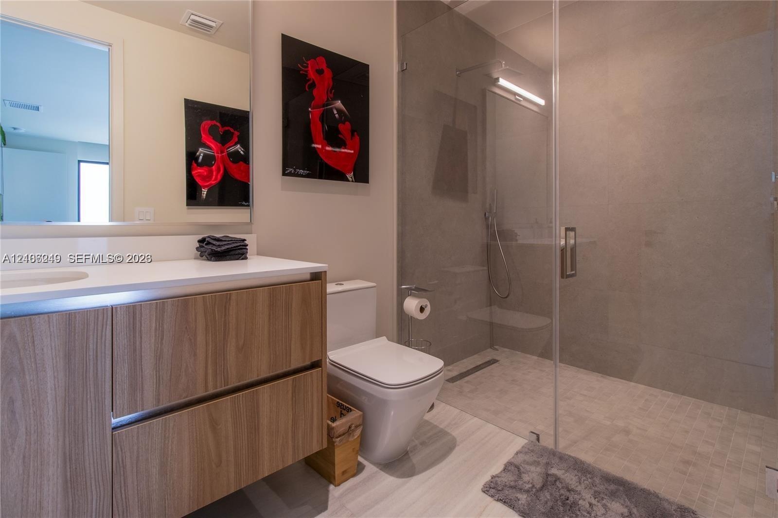 Modern bathroom featuring a wood-finish vanity with a white countertop, walk-in shower with floor-to-ceiling tile, frameless glass enclosure, and a wa