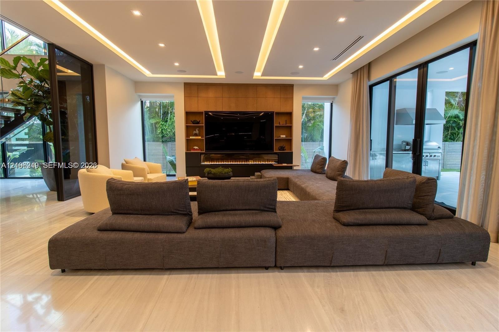 Living area featuring a coffered ceiling with integrated cove lighting, recessed lighting, polished stone flooring, a full-height wood-paneled media w