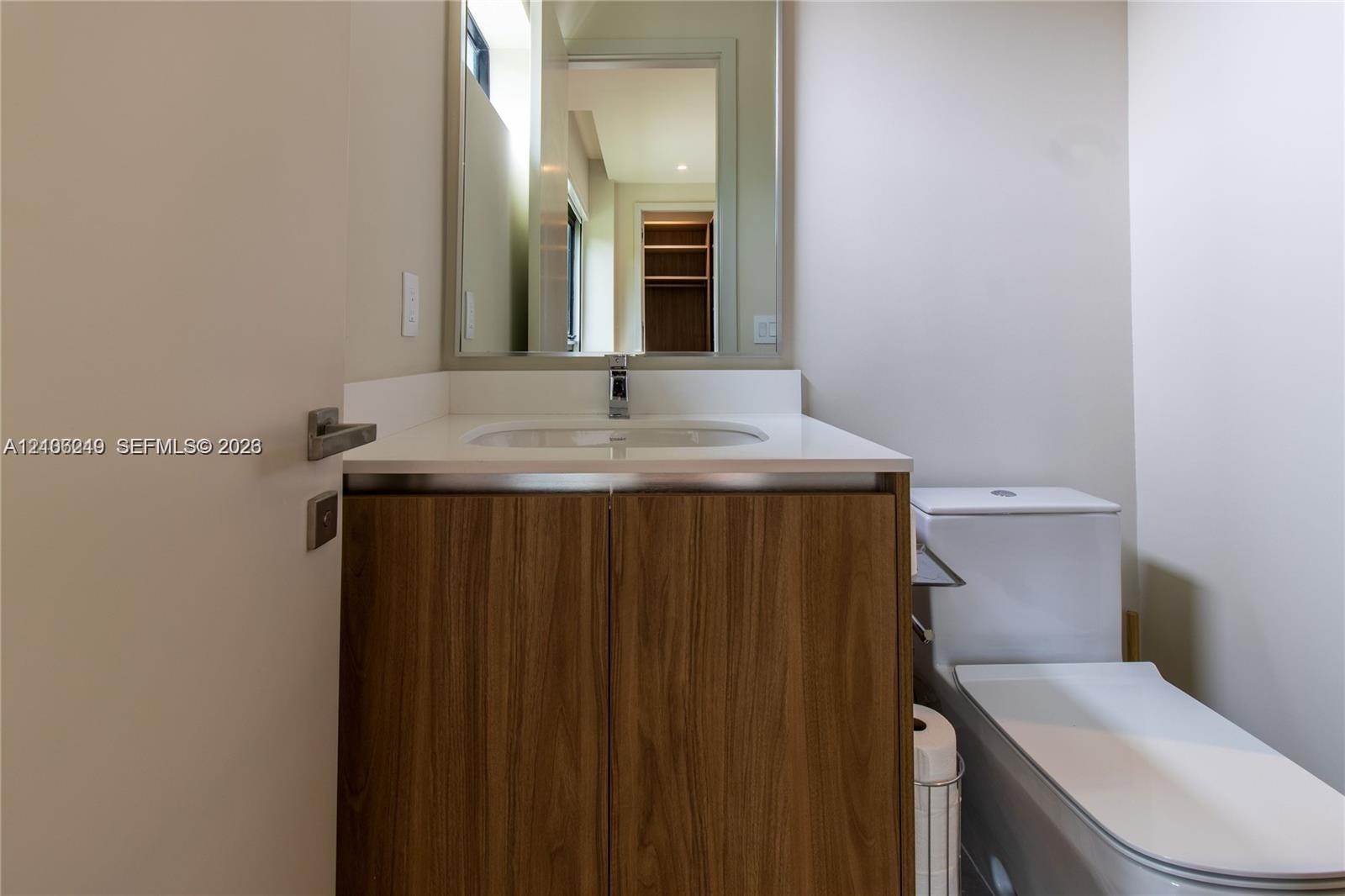 Vanity featuring a wood-finish cabinet, white countertop with an integrated basin, wall-mounted mirror, and chrome faucet