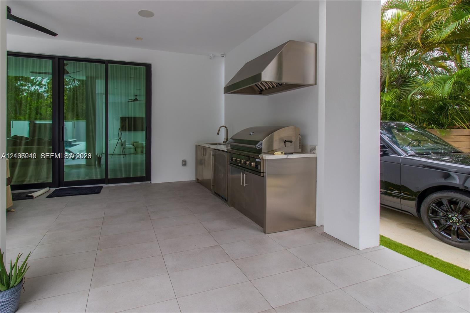 Covered outdoor kitchen featuring stainless steel cabinetry, built-in grill, professional-grade range hood, stone-surface countertop, and large-format