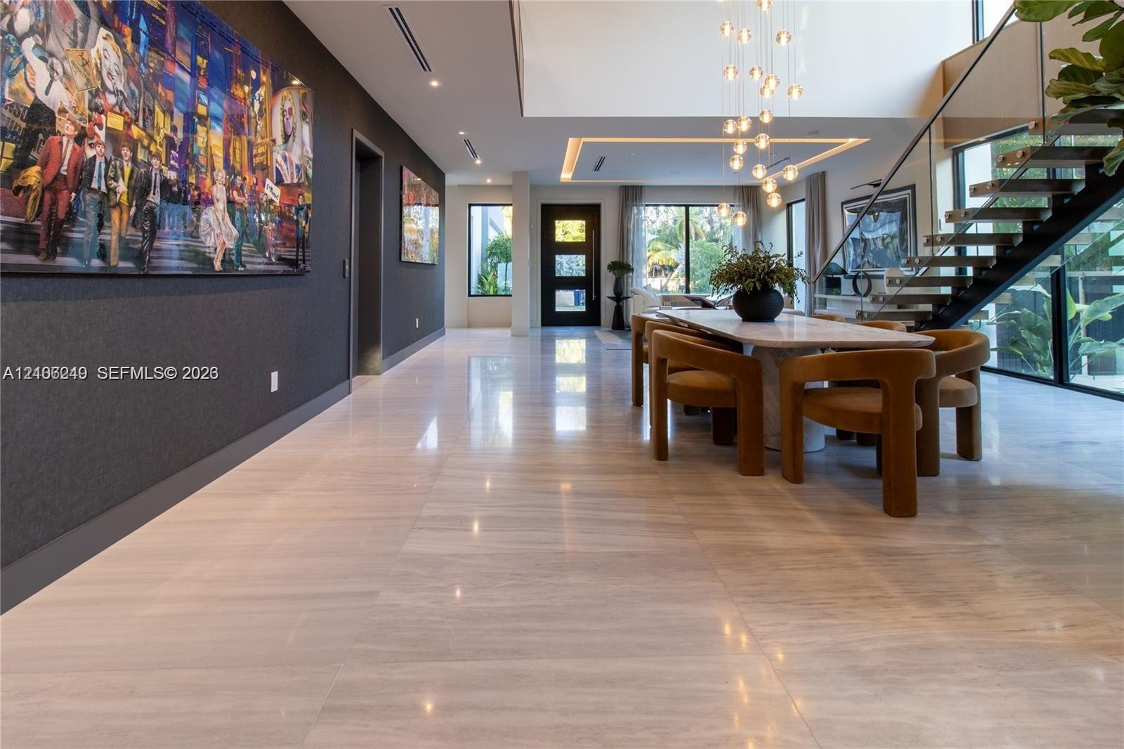 Open-concept interior featuring large-format tile flooring, a double-height ceiling with recessed cove lighting, and a suspended staircase with glass 