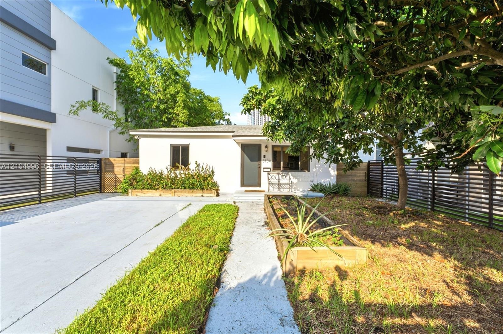 Single-story residence featuring a smooth stucco exterior, a concrete driveway, horizontal slat perimeter fencing, and raised wooden planter boxes