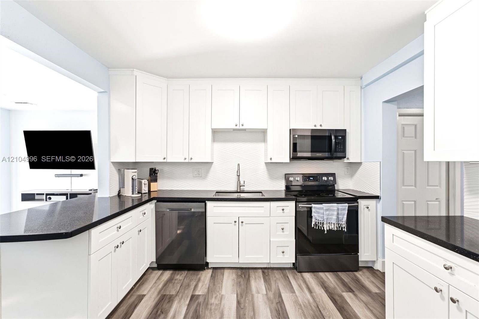 Kitchen featuring white shaker-style cabinetry, dark stone-finish countertops, black appliances, a textured tile backsplash, and wood-finish flooring