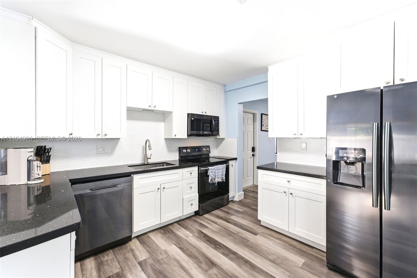 Kitchen featuring white cabinetry, dark stone-finish countertops, textured tile backsplash, stainless steel appliances, and wood-finish flooring