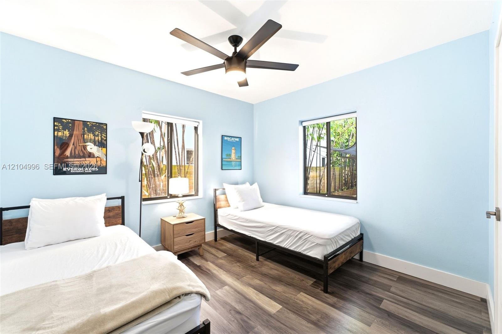 Interior room featuring wood-finish flooring, two dual-pane windows, and a matte black ceiling fan