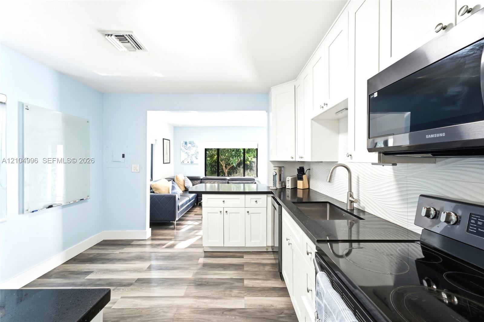Kitchen featuring white shaker-style cabinetry, dark stone countertops, stainless steel appliances, a textured tile backsplash, and wood-finish floori
