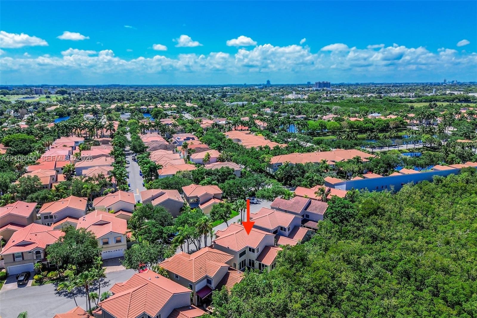 Aerial perspective of a multi-story residence featuring a tile roof, light-toned exterior finish, and a concrete driveway situated within a landscape 