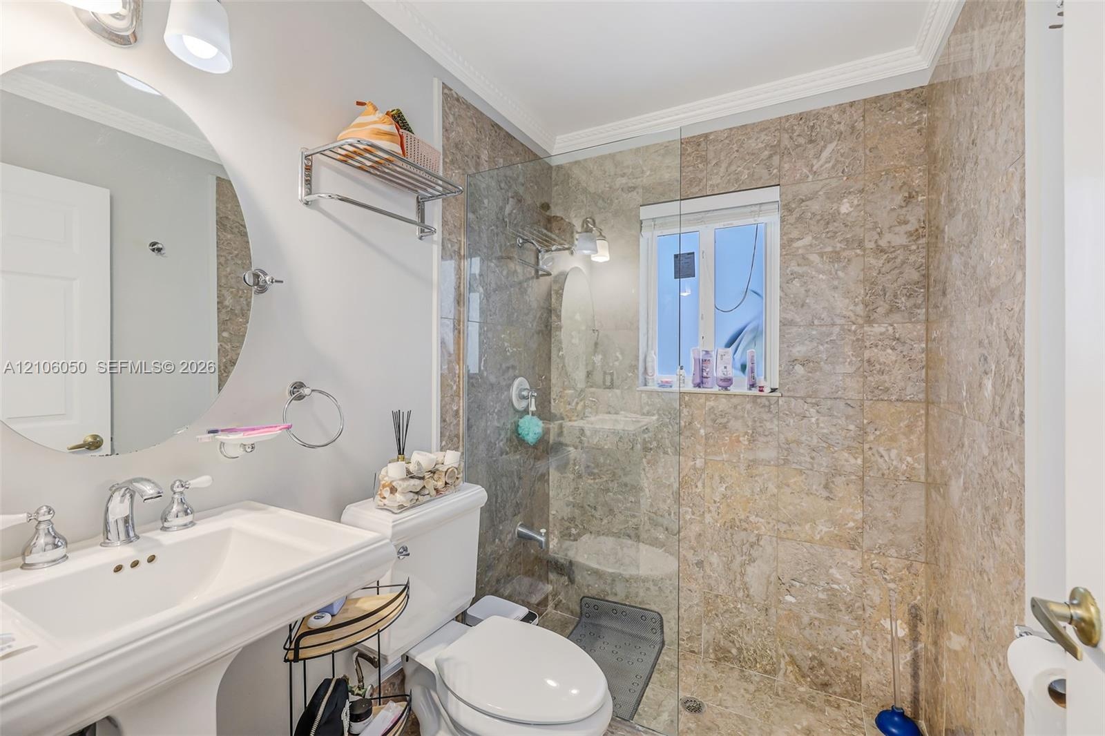 Bathroom featuring a wall-mounted oval mirror, porcelain pedestal sink, chrome hardware, and a glass-enclosed walk-in shower finished with full-height