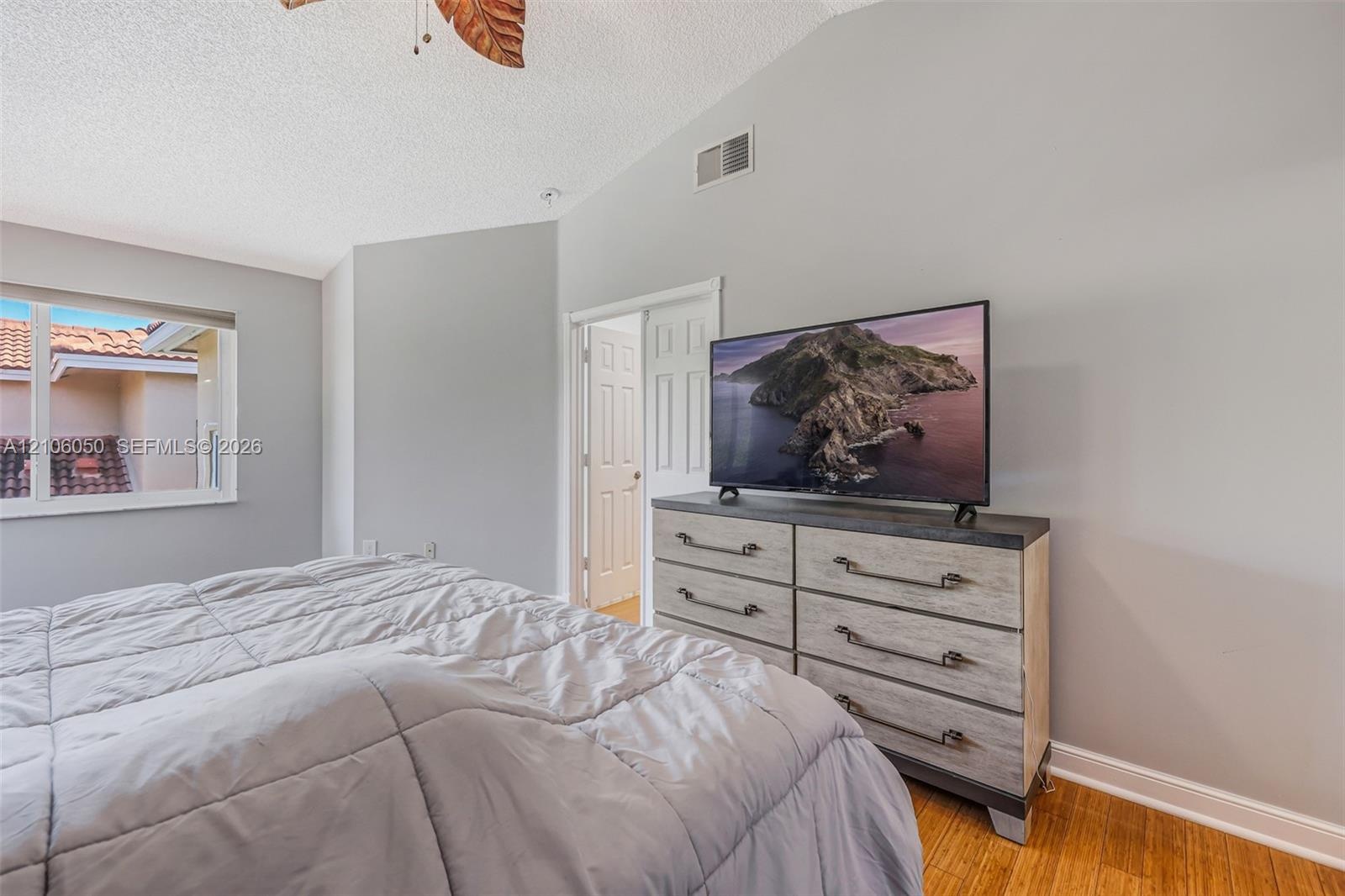 Vaulted ceiling with a ceiling fan, neutral wall paint, wood-finish flooring, and single-hung window with a view of exterior tile roofing