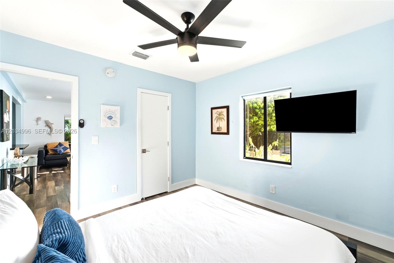 Room featuring light blue walls, a dark-finish ceiling fan with an integrated light fixture, a single-pane window, and a white interior door