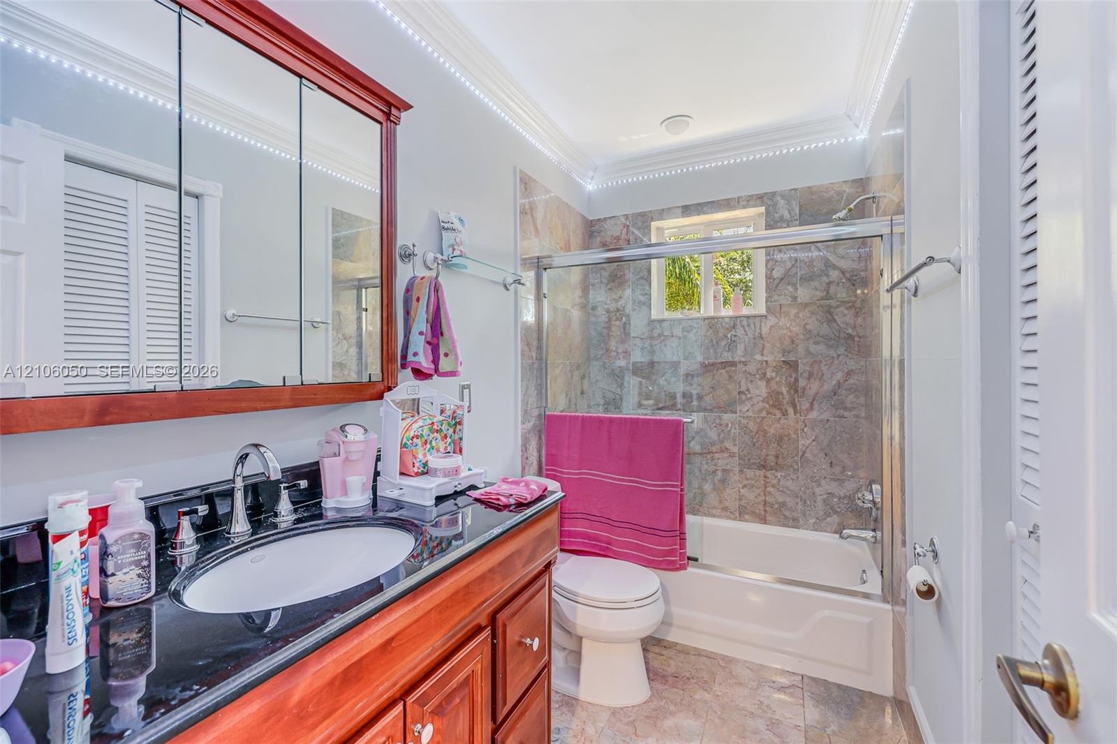 Bathroom featuring a wood-finish vanity with a dark polished countertop, undermount sink, multi-panel medicine cabinet, and a bathtub enclosure with s