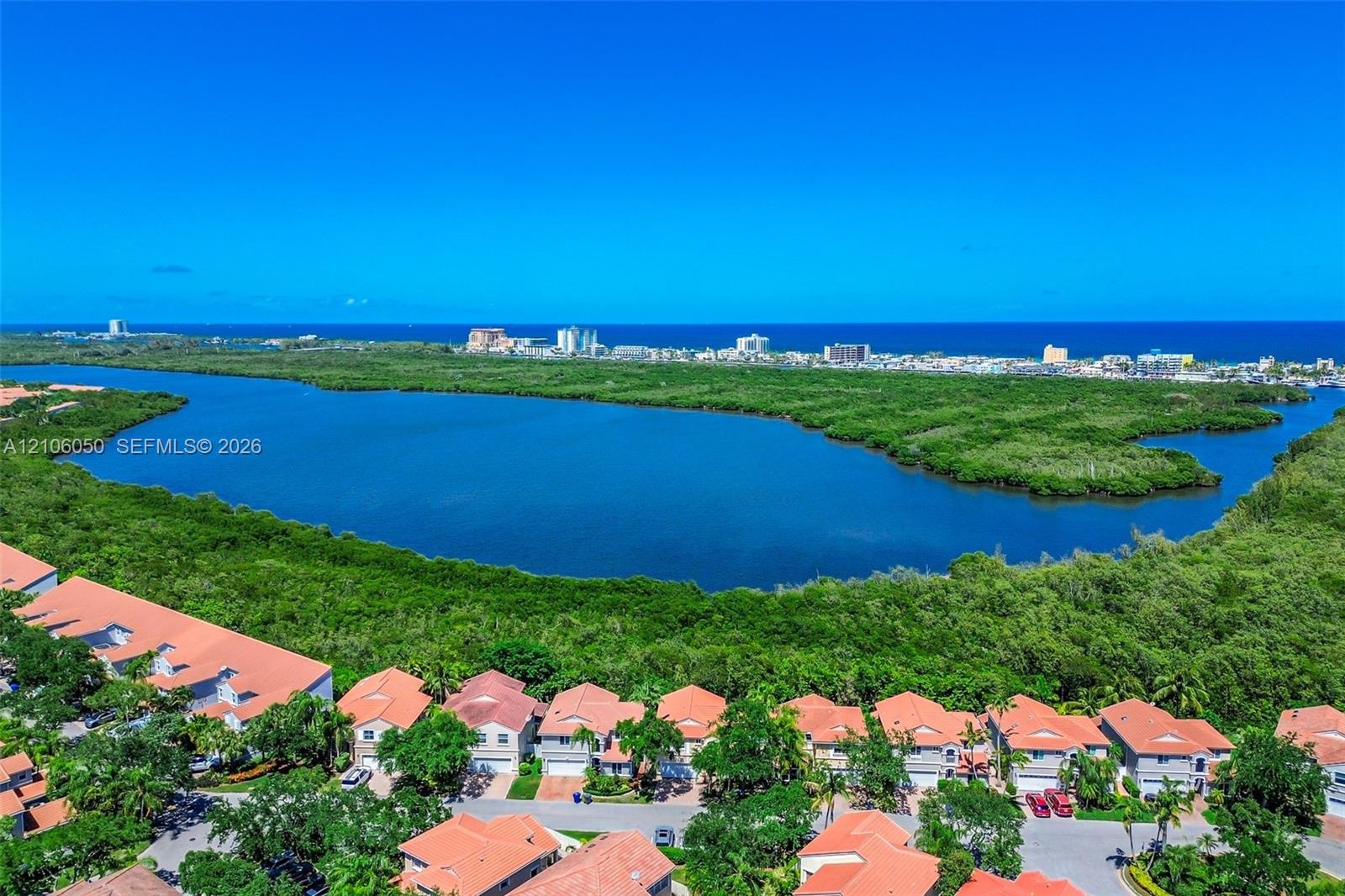 Aerial perspective featuring residential structures with clay-tile roofs, expansive mangrove preserve, and coastal horizon