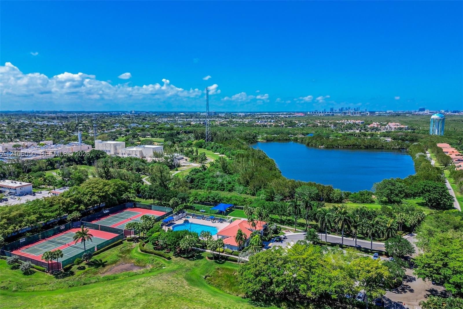Aerial perspective featuring a community swimming pool, two hard-court tennis surfaces, and a large lake