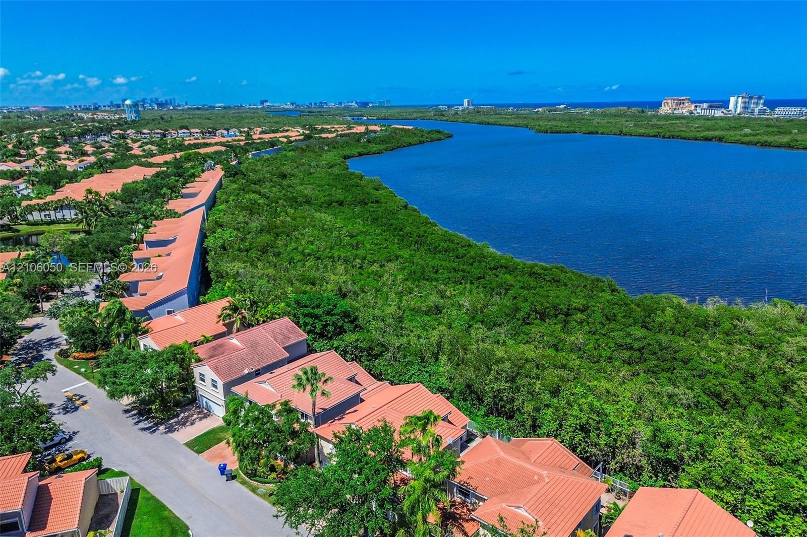 Aerial perspective featuring clay tile roofing, asphalt paving, and coastal waterway proximity with native vegetation