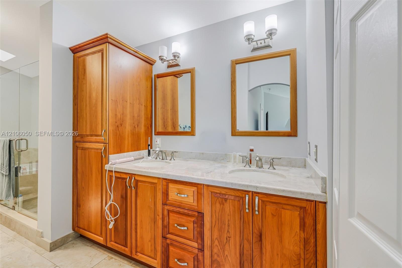Double vanity featuring a light-toned stone countertop, wood cabinetry with integrated floor-to-ceiling storage, two wall-mounted mirrors with wood fr