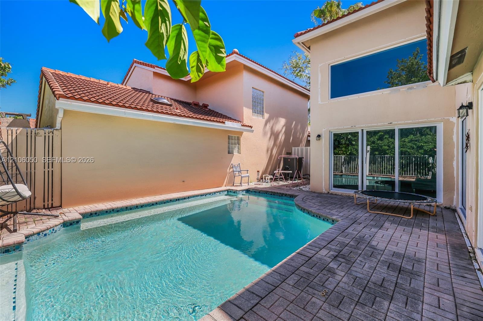 Stucco exterior with a tiled roof featuring an in-ground swimming pool and expansive paver patio