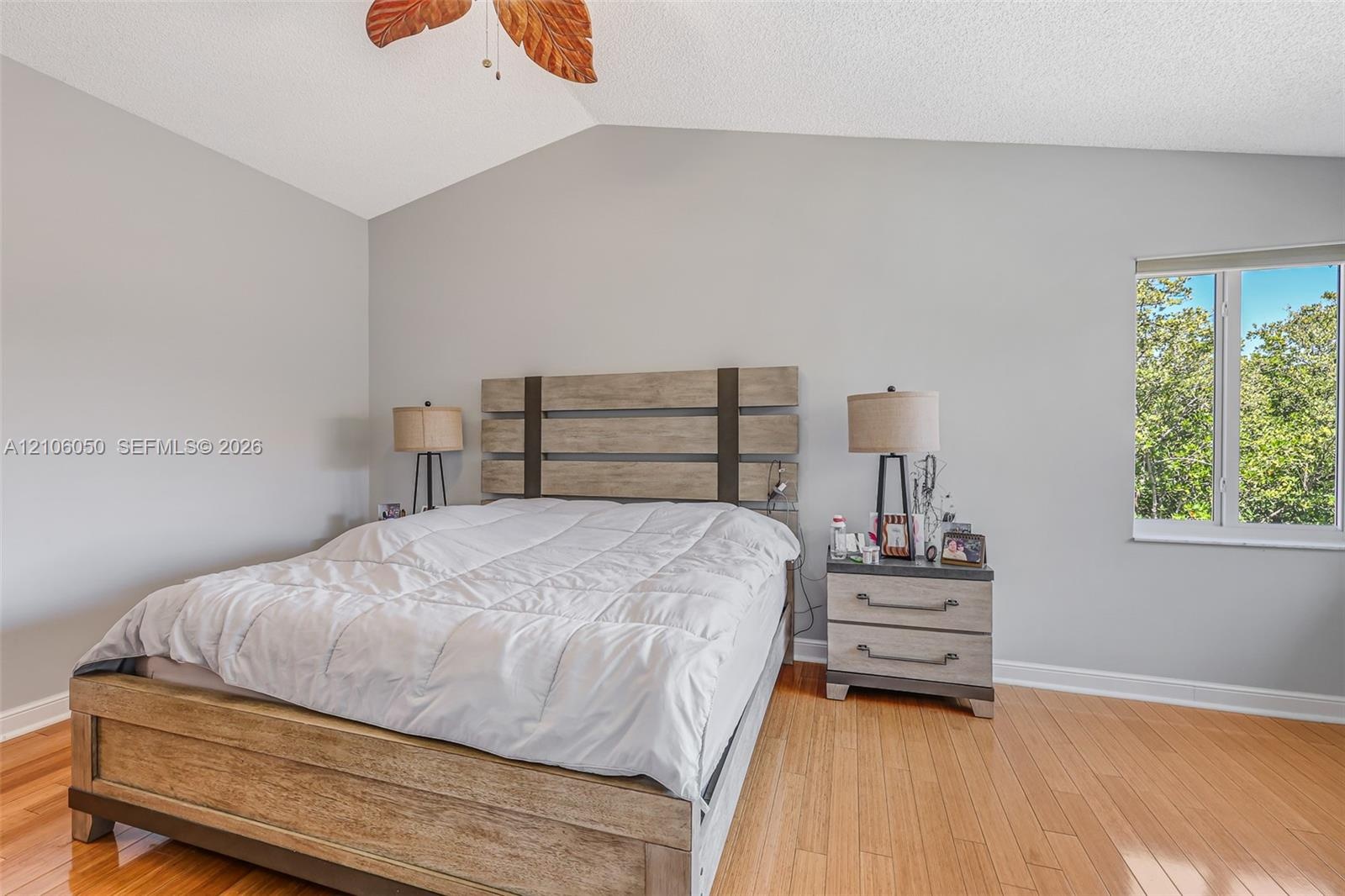 Vaulted ceilings, wood-finish flooring, and natural light from a window with exterior greenery