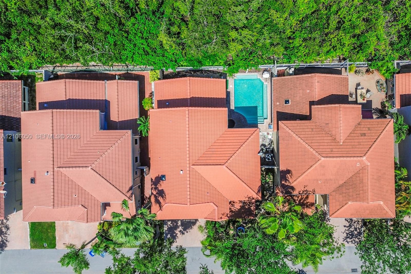 Aerial perspective of multi-structure property featuring red clay tile roofing, private swimming pool, paved patio, and mature perimeter landscaping