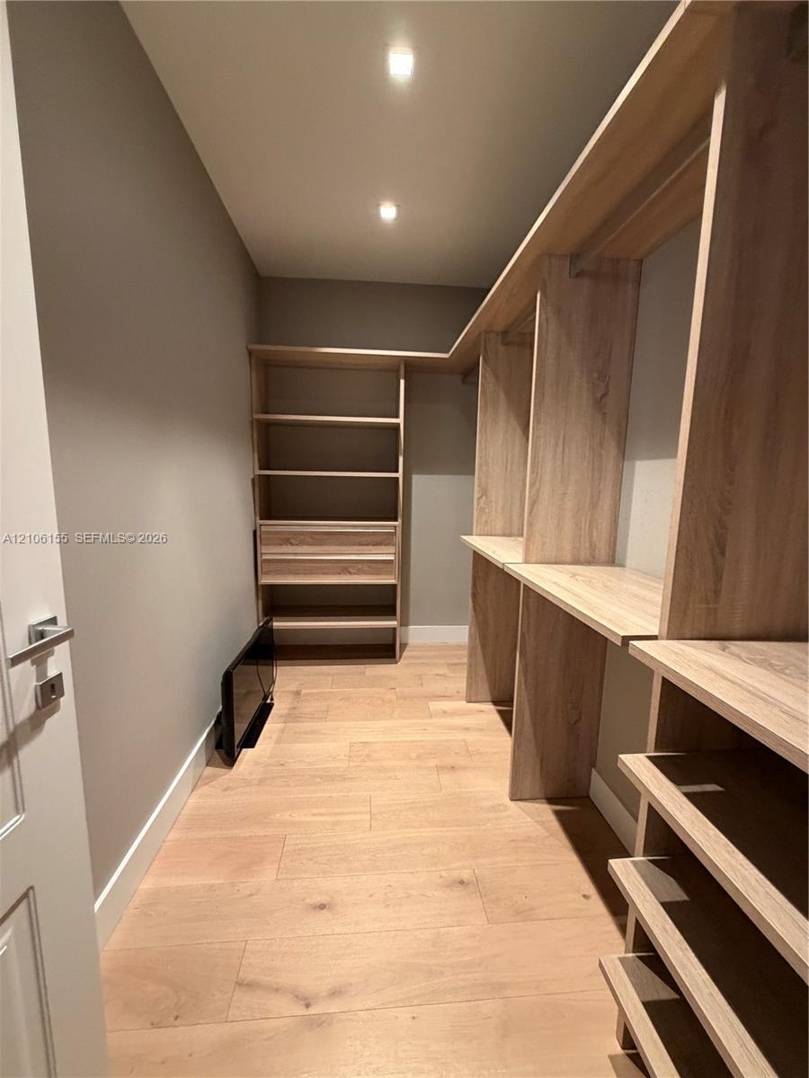 Custom walk-in closet featuring light-toned wood-finish built-in shelving, integrated hanging rods, built-in storage drawers, and wood-finish flooring